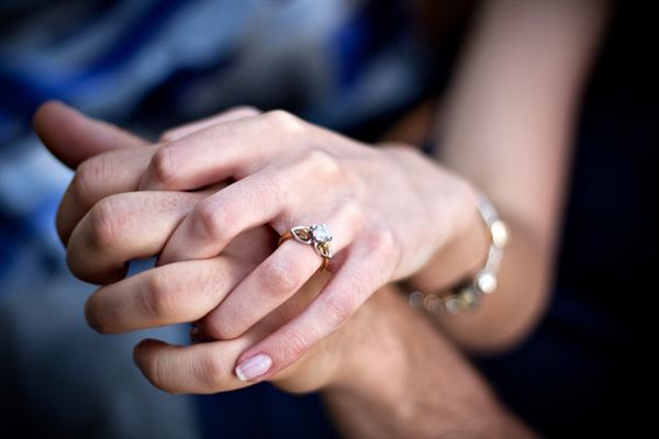 Woman with a unique engagement ring holding her fiancé's hand.